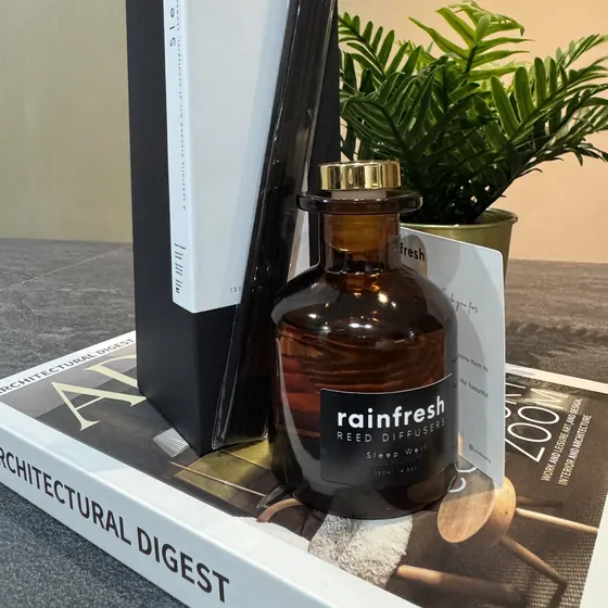 Reed diffuser in its amber glass bottle with black reeds, next to its gift box