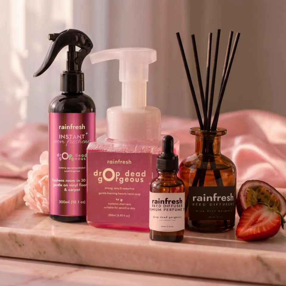 Drop Dead Gorgeous collection — room freshener, hand soap, perfume oil and reed diffuser — on a marble tray with a peony, passionfruit and strawberry, sheer curtains behind