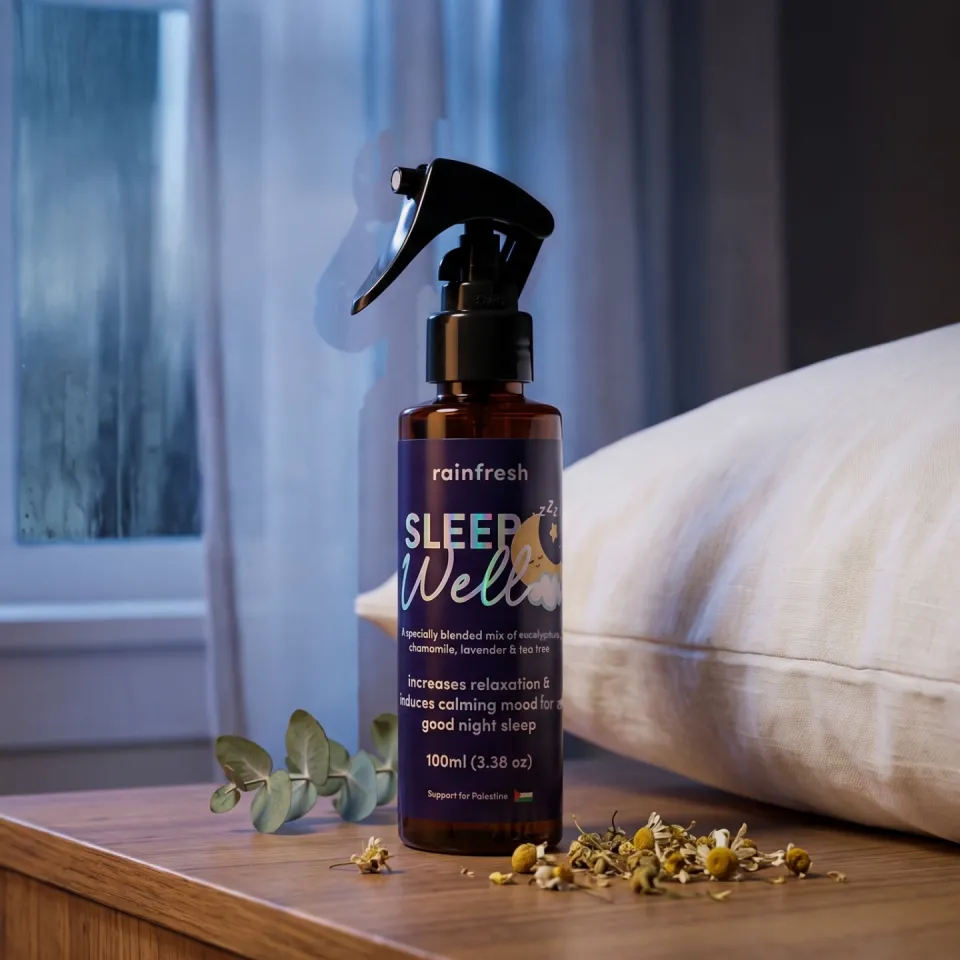 Sleep Well spray on a bedside table with eucalyptus and dried chamomile, a pillow and rainy window behind